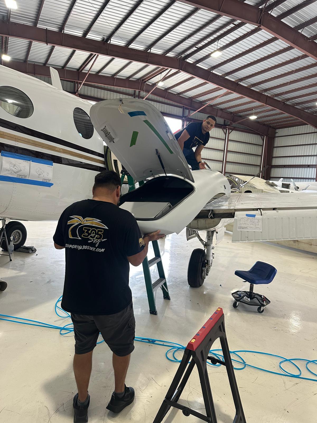 305 Sky technicians in branded shirts lifting an engine cowling clear of a King Air.