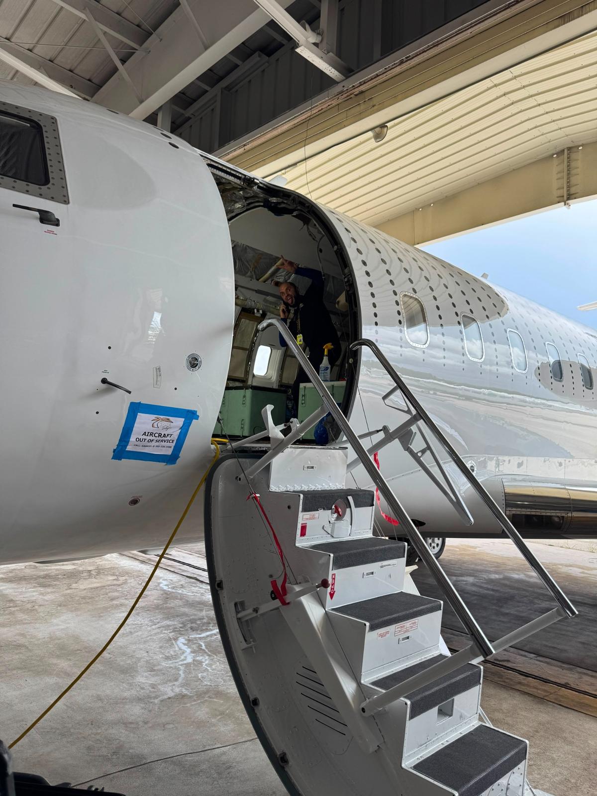 305 Sky aircraft-out-of-service placard taped beside the open entry door of a Bombardier jet.