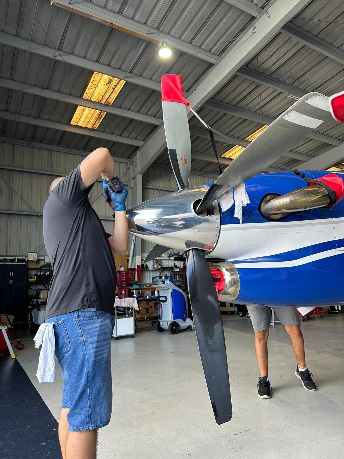 Two technicians fitting a propeller assembly to the spinner of a blue and white turboprop.