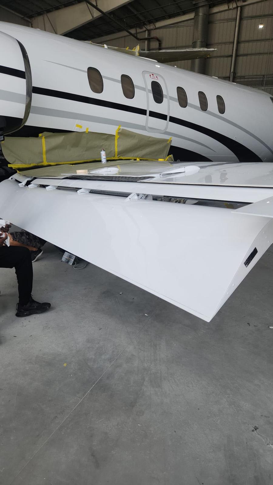 Technician working beneath a masked business jet wing during panel refinishing.