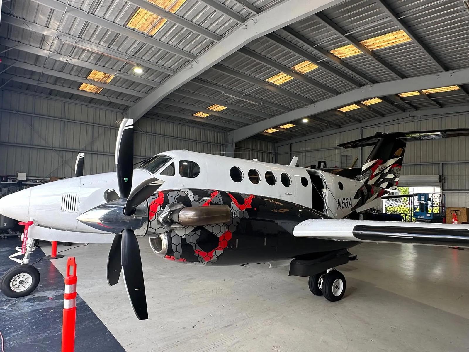 Beechcraft King Air N56A in the hangar wearing a red, grey and black hexagonal camouflage scheme.