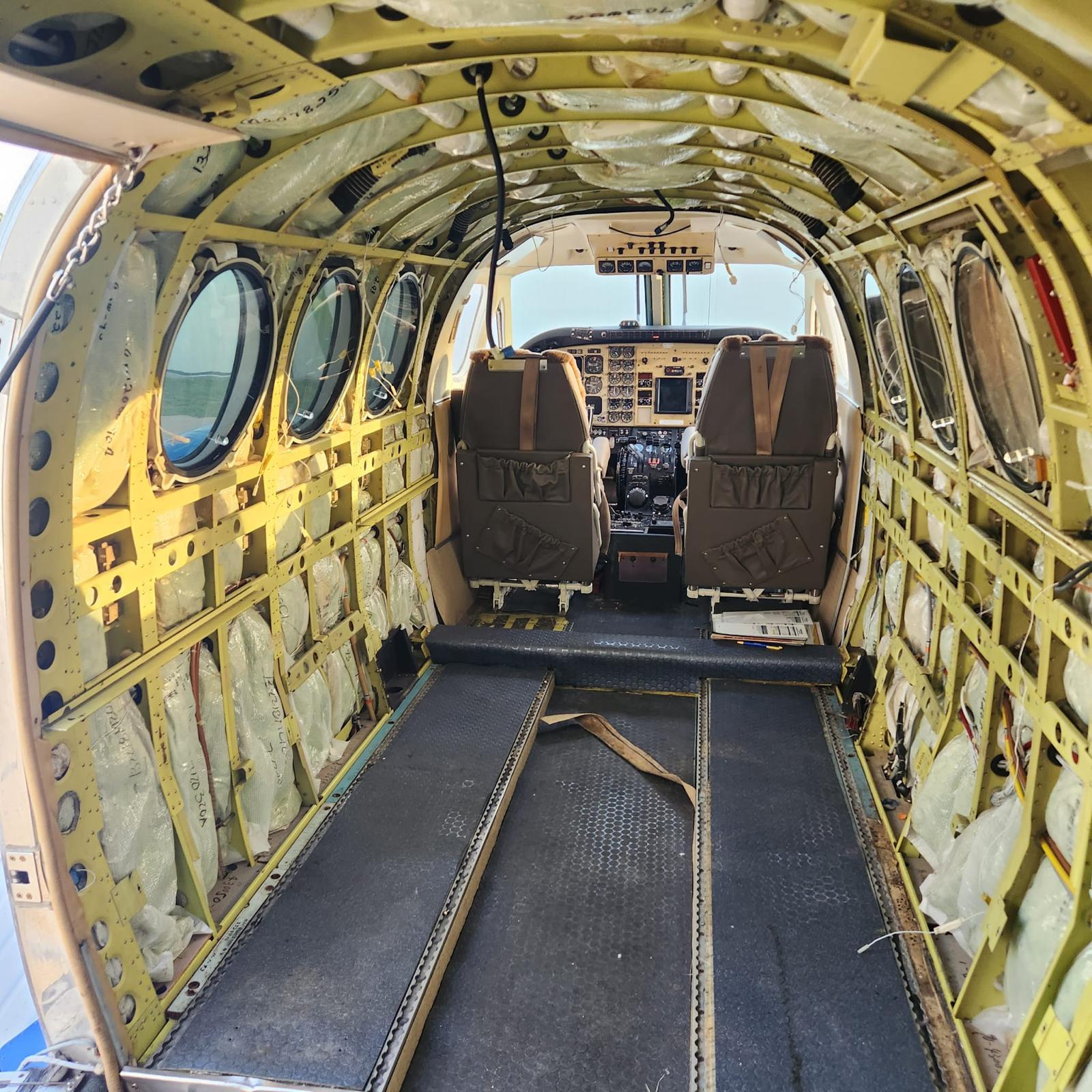 King Air cabin stripped to bare primed frames with insulation bags exposed and all trim removed.