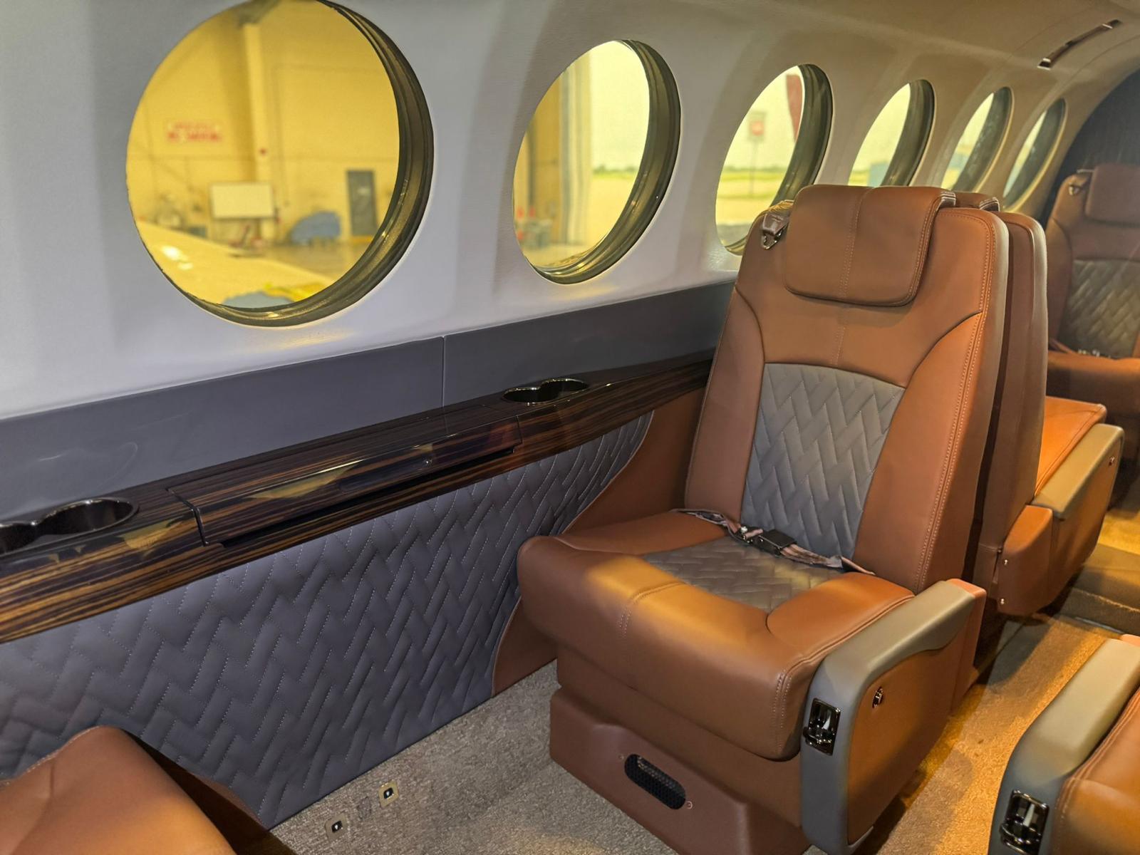 Close view of a quilted tan and grey leather cabin seat beside a polished ebony veneer sidewall rail.