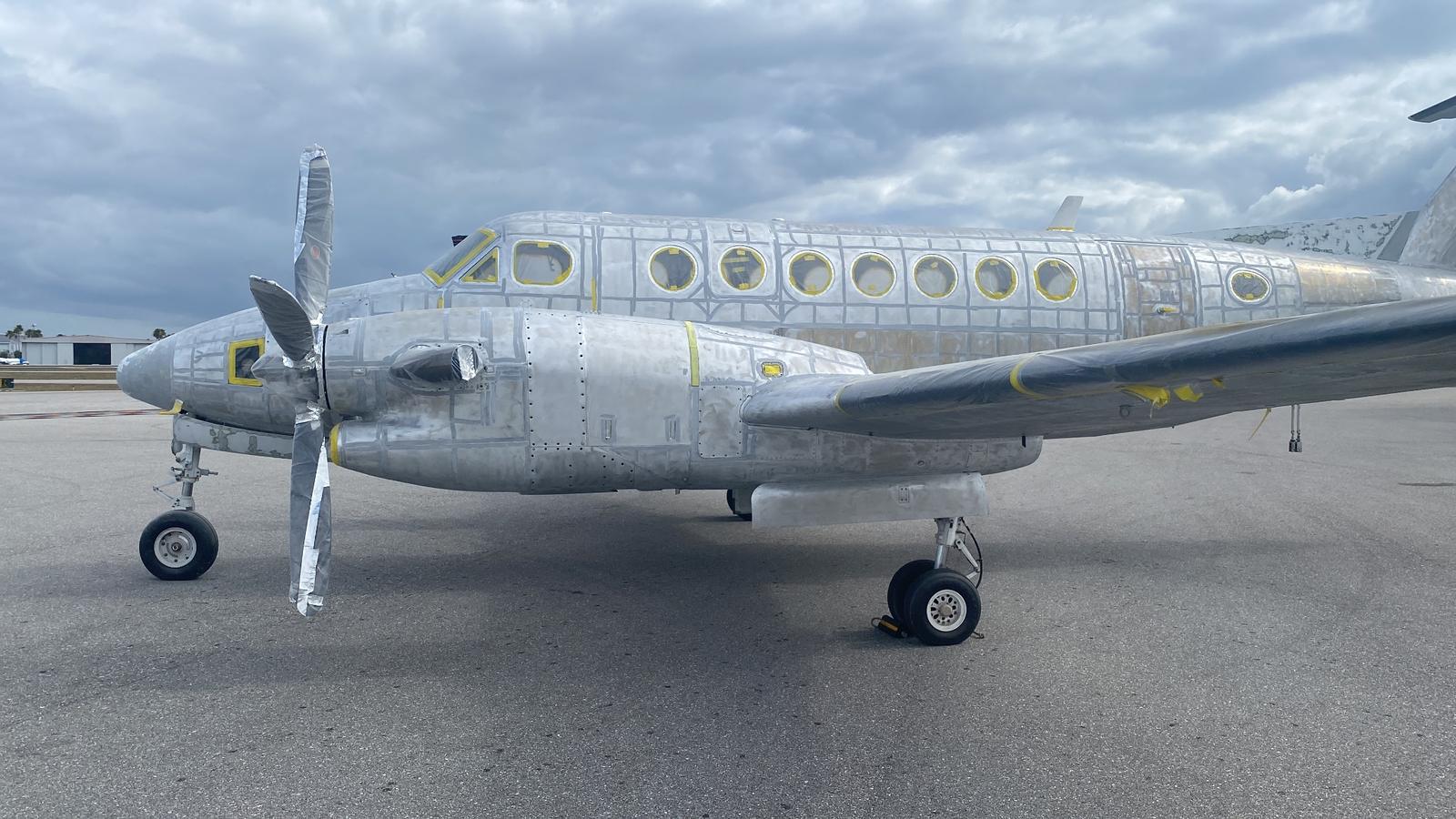 King Air N222PV stripped to bare aluminium on the ramp with windows and propellers masked.